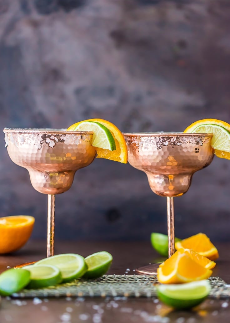 two margaritas surrounded by slices of lime and orange