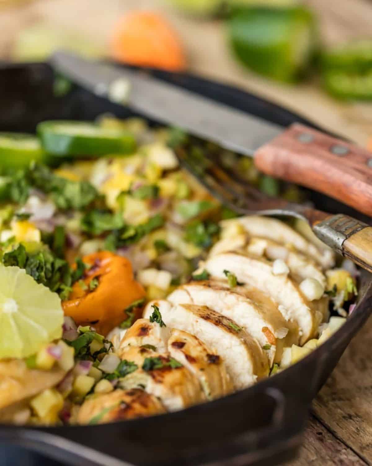 Jerk Chicken with Mango Salsa is a surprisingly easy dish. Make this One Pan Caribbean Jerk Chicken recipe in just 15 minutes! Pair this flavorful chicken with rice for a delicious and easy weeknight meal! One Pan Caribbean Jerk Chicken with Mango salsa in a skillet with a fork.
