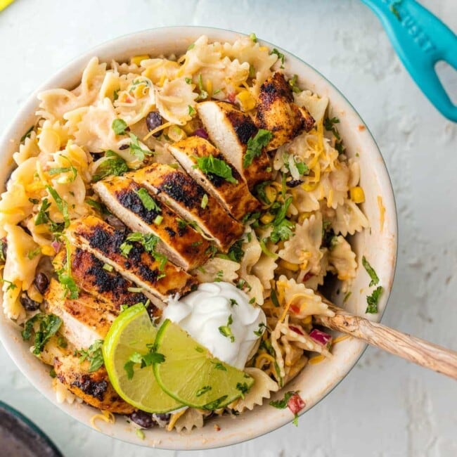 Chicken Enchilada Pasta Salad is bursting with flavor, super easy, and sure to please! Make it as indulgent or healthy as you'd like, you can't go wrong! Loaded with corn, beans, taco spiced chicken, onion, cilantro, and cheese. YES PLEASE!