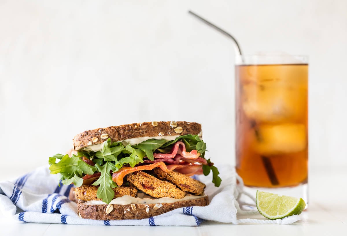 A blt sandwich on a dish towel next to a glass of sweet tea