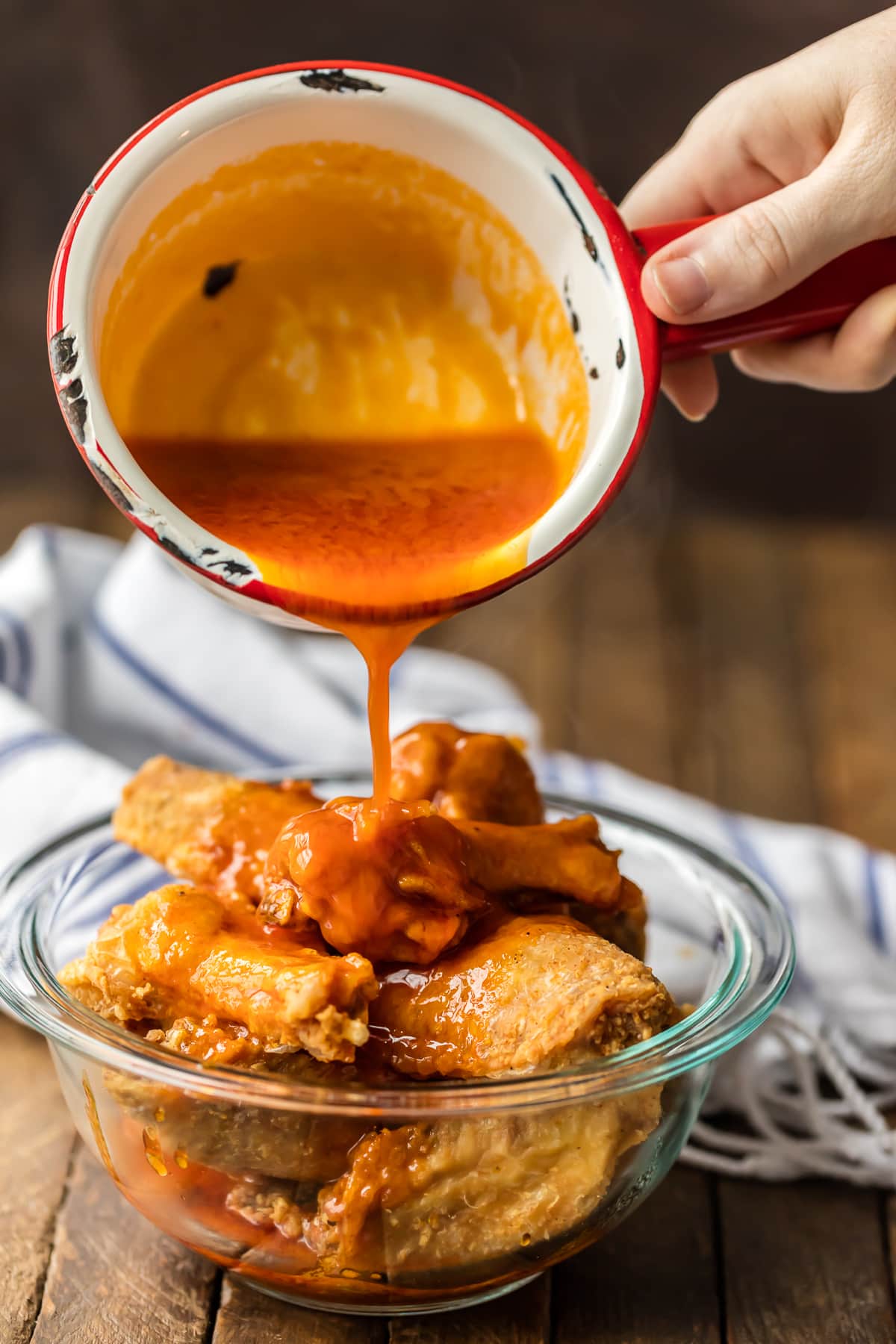 Pouring hot sauce over fried buffalo wings in a bowl