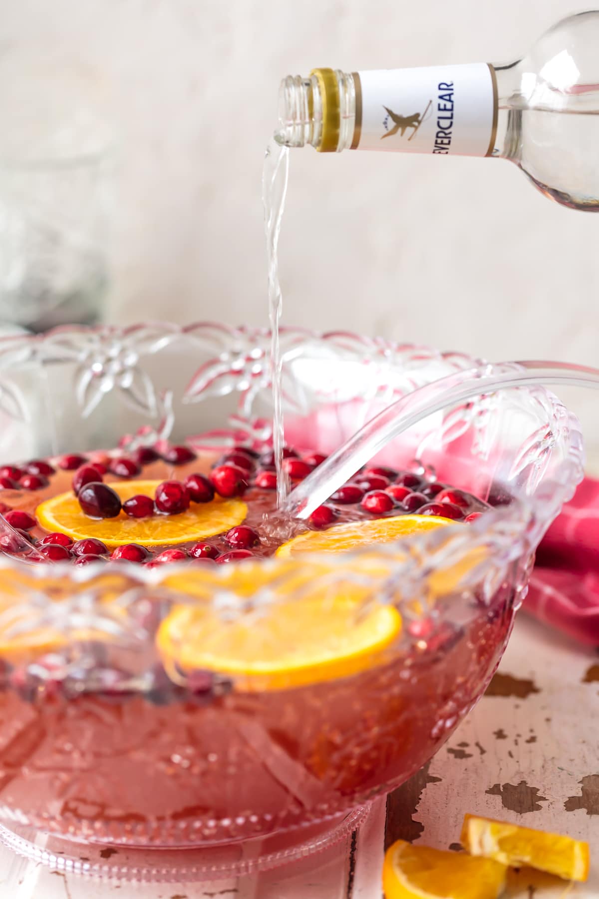Holiday Punch is one of our favorite EASY PUNCH RECIPES perfect for Thanksgiving or Christmas! This Vodka punch is made with Cranberry Juice, Orange Juice, Ginger Ale, Sparkling Cider and more! You can pour in the Vodka or make it your new Non Alcoholic Christmas Punch Recipe. One of our very favorite Holiday Punch Recipes. pouring vodka into christmas punch