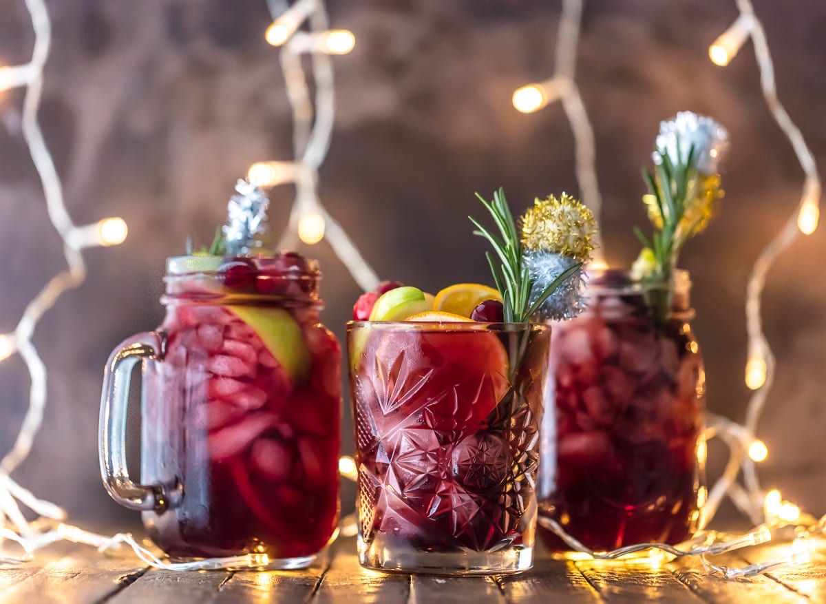 HOLIDAY SANGRIA is the perfect Christmas cocktail! It's made with red wine, vodka, sparkling apple cider, and several juices. Better yet, this Christmas Sangria is gluten free. You'll be the star of any holiday party with this recipe. Cheers! Three glasses of Christmas Sangria, garnished with rosemary and fruit