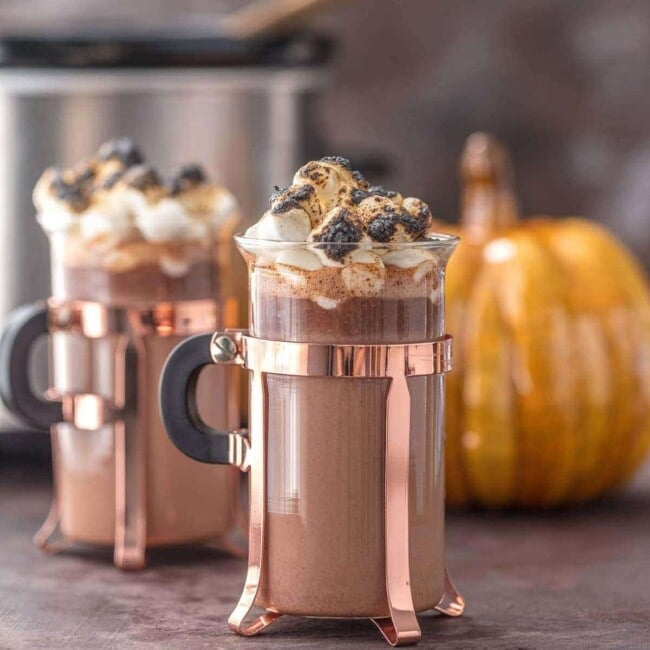 mugs of spiked hot chocolate in front of a pumpkin