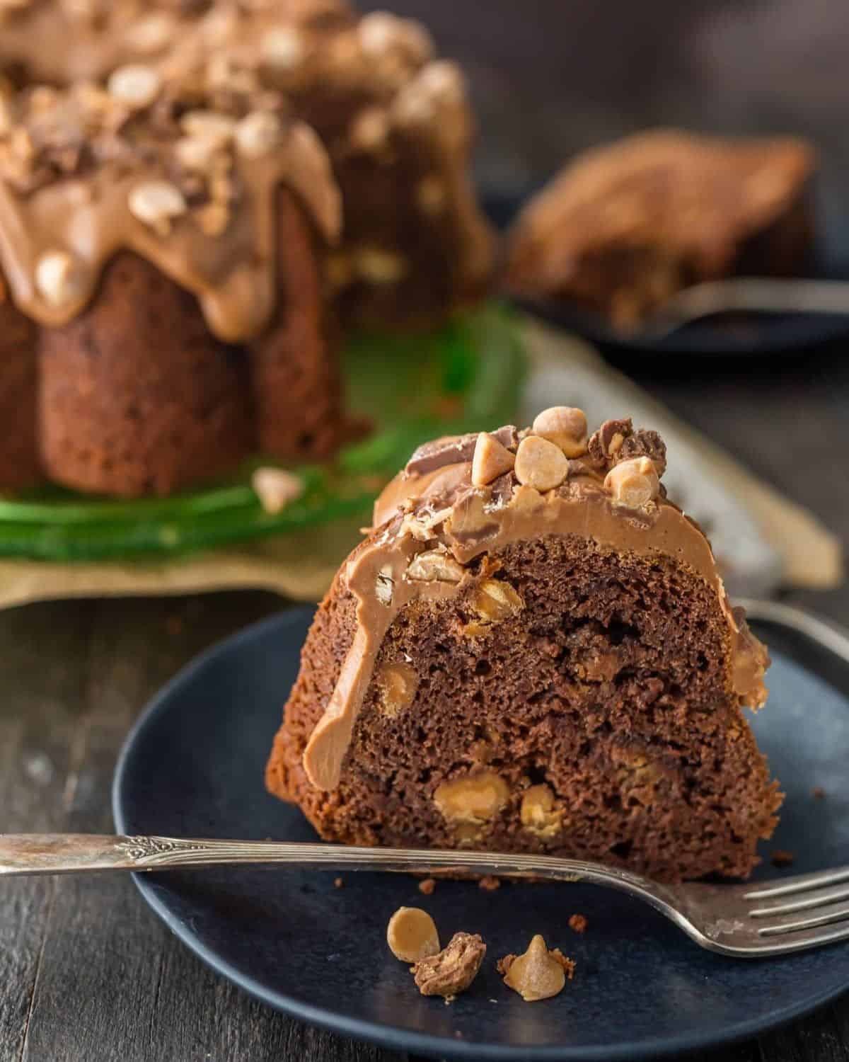 This CHOCOLATE PEANUT BUTTER CAKE is the ultimate bundt cake recipe! The cake is made with peanut butter AND peanut butter cups, and then topped with a decadent peanut butter icing. All that peanut butter makes this indulgent cake the most amazing peanut butter chocolate cake recipe! A slice of chocolate peanut butter cake with peanut butter frosting on a plate with a fork.