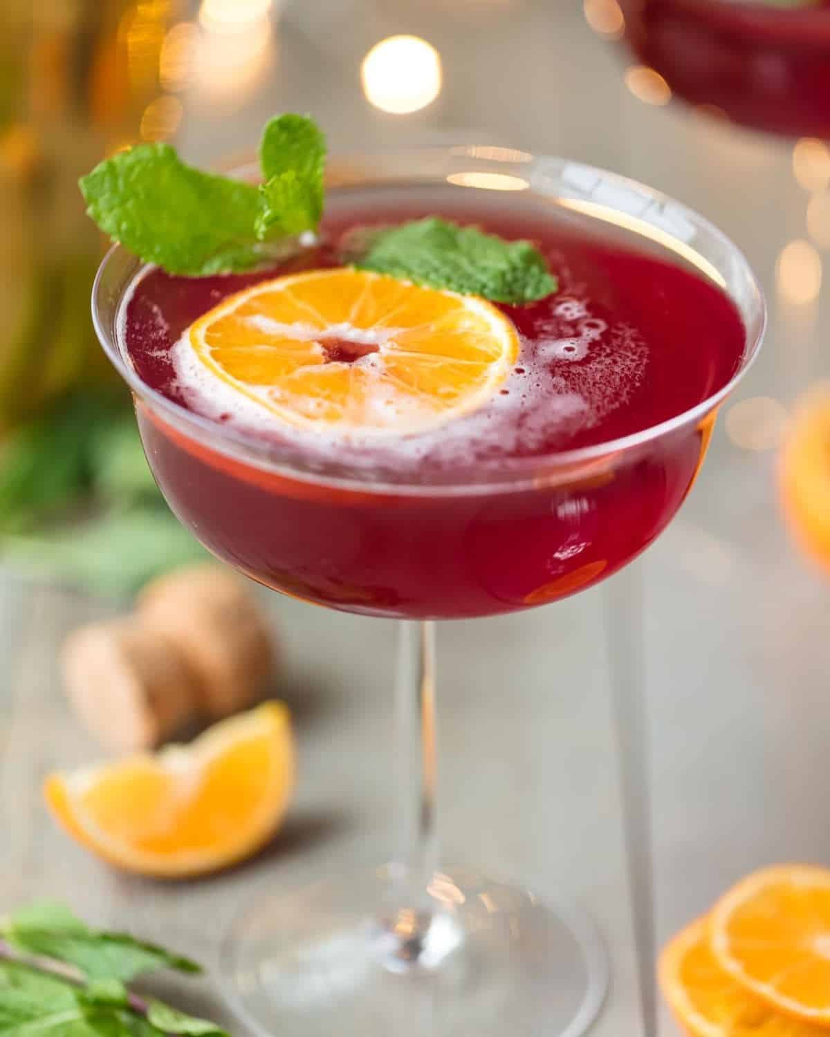 Flirtinis are a fun drink perfect for festive occasions. This Sparkling Holiday Flirtini is so fun, so pretty, and so delicious! It's made from cranberry and pineapple juice mixed with orange vodka, and topped off with red Moscato champagne. It's the perfect holiday cocktail recipe for Christmas or New Year's Eve! Sparkling holiday flirtini in a martini glass garnished with an orange slice and fresh mint.