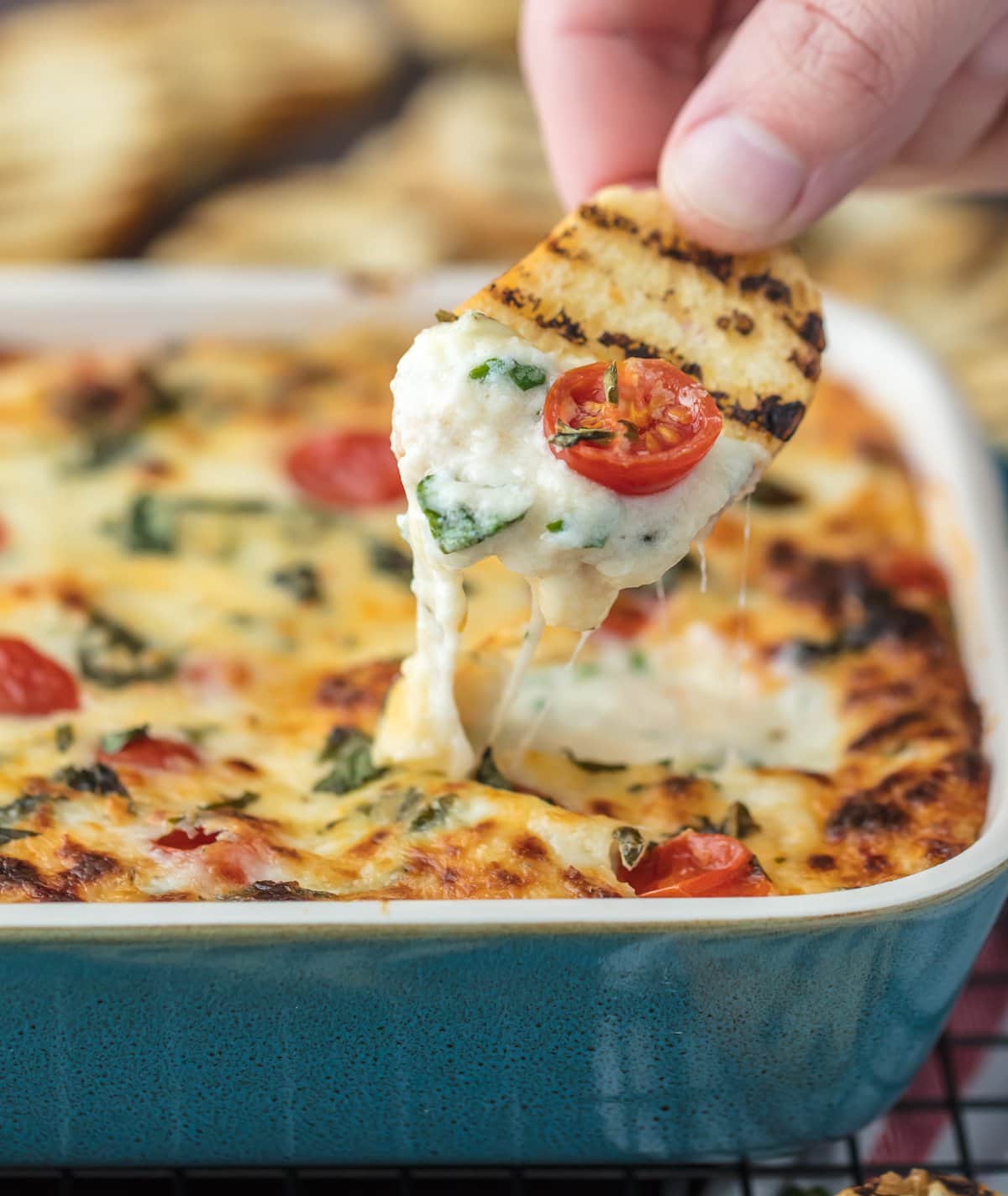 Dipping toasted bread into cheesy caprese dip