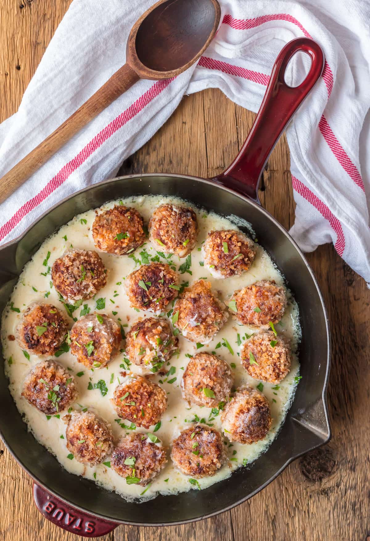 Cordon Bleu Chicken Meatballs in a skillet, next to a dish towel and a wooden spoon