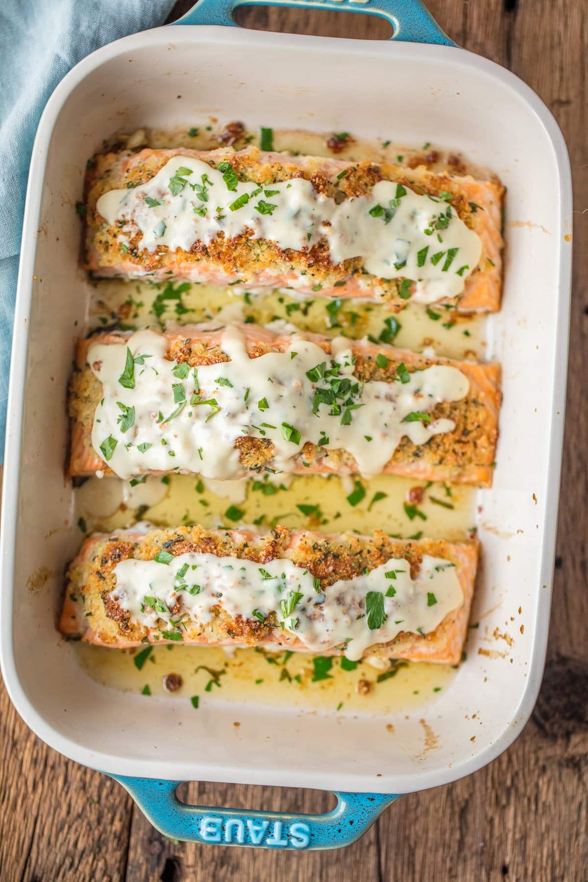 Parmesan Salmon in a baking dish topped with creamy white wine sauce