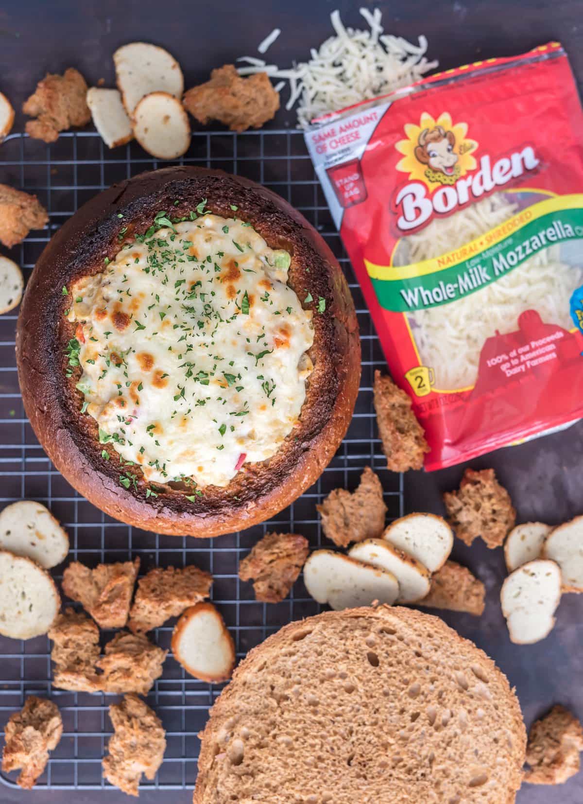 Cheesy bread bowl dip next to a package of shredded cheese