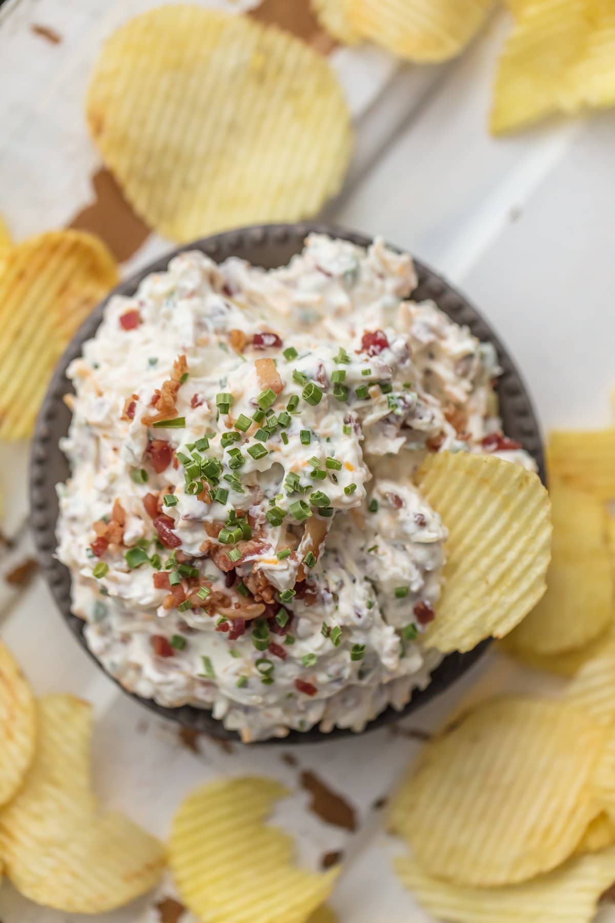 A bowl of caramelized onion bacon dip, surrounded by ruffled potato chips