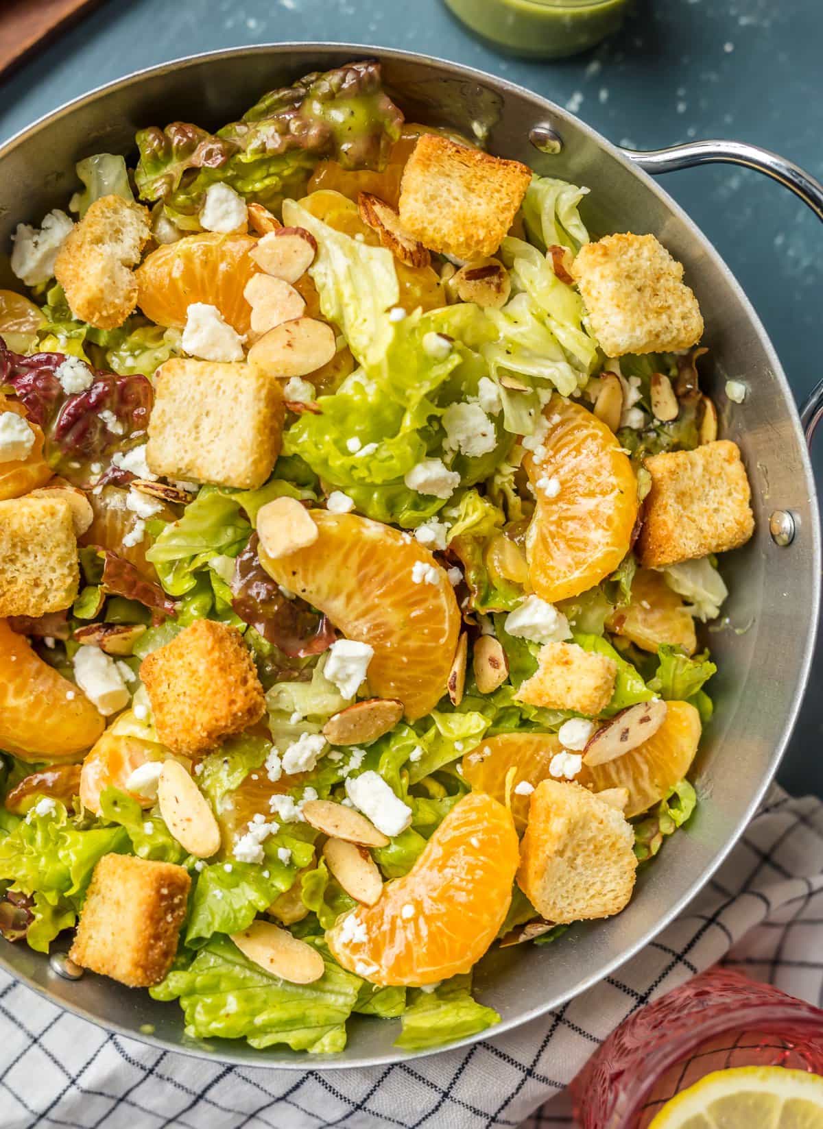 Large silver bowl filled with lettuce, mandarin oranges, almonds, and feta