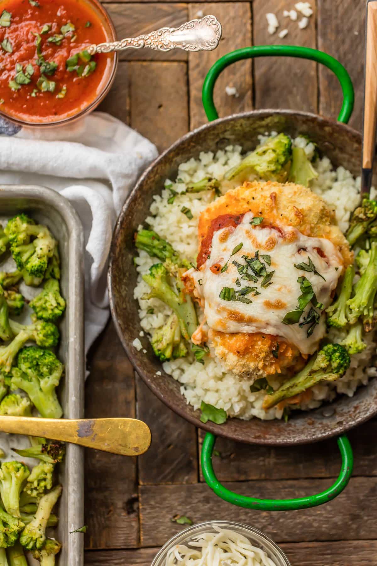 A bowl of riced cauliflower topped with baked chicken breast and broccoli