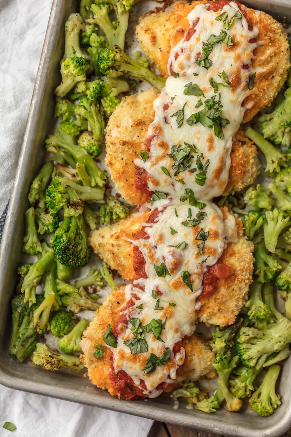 Chicken parmesan on a sheet pan topped with cheese, surrounded by roasted broccoli