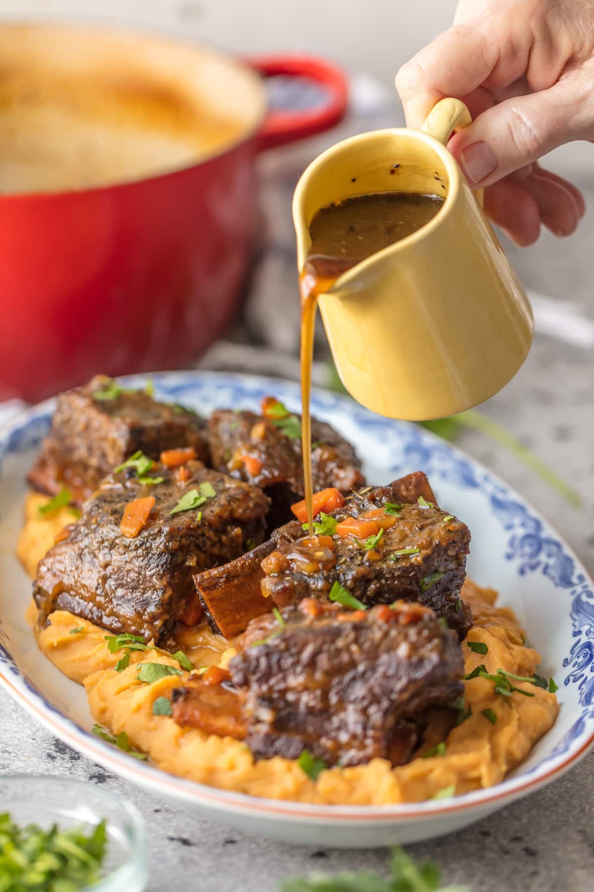 Pouring honey bourbon glaze over plate of short ribs