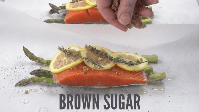 2 salmon filets on top of asparagus and topped with lemon slices, thyme, and brown sugar.