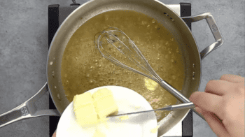butter pushed by a knife from a white plate into a saucepan with a whisk.