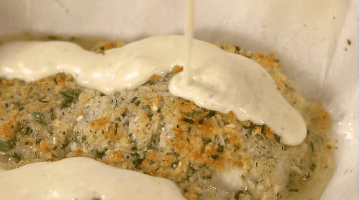 white wine dijon cream sauce drizzled over parmesan crusted salmon filets in a baking pan.