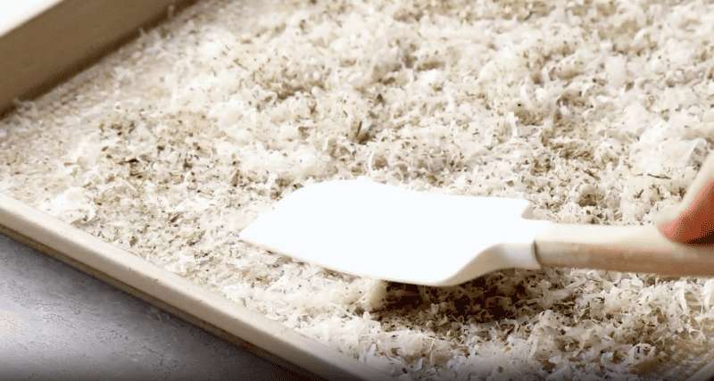 A person using a spatula to spread shredded parmesan on a baking sheet for parmesan potato wedges.