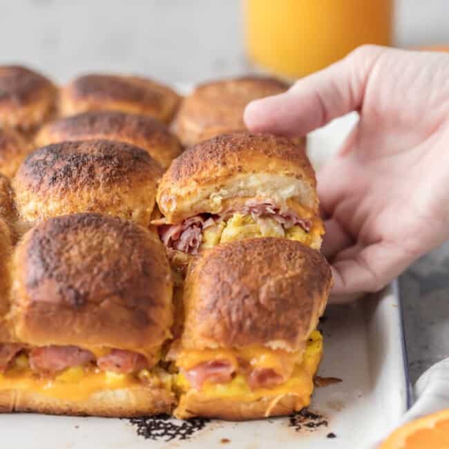 These CHEESY BAKED BREAKFAST SLIDERS are so easy and perfect for feeding a crowd! Baked on Hawaiian rolls with layers of ham, egg, and cheese and topped with a brown sugar dijon butter sauce! TOO GOOD!
