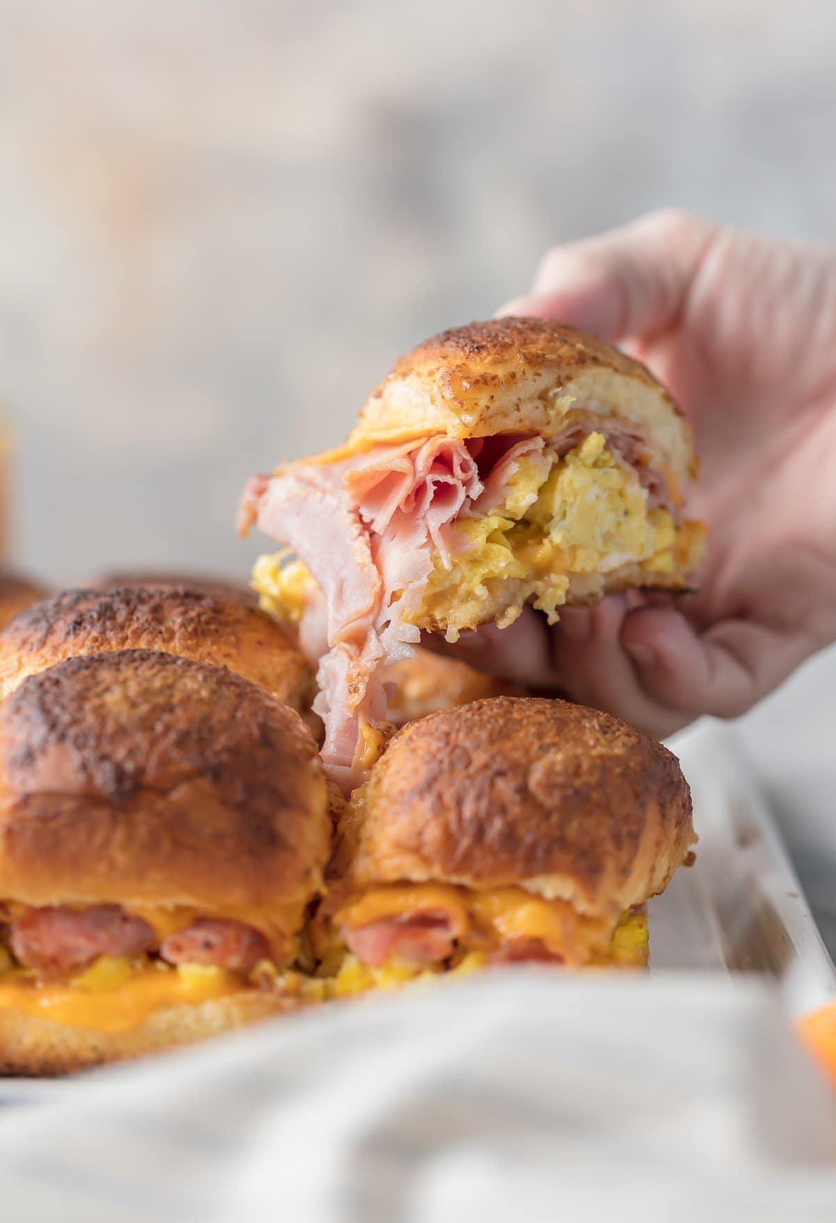 A hand picking up an egg, ham, and cheese slider