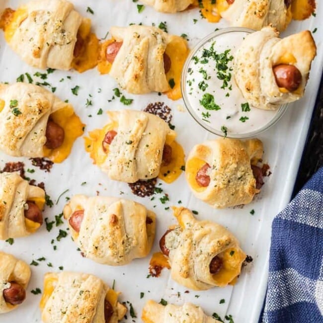 Pigs in a Blanket with Cheese and Parmesan Ranch Butter will be all the rage at your next party. This Pigs in a Blanket Recipe is easy, fun, and oh so delicious. If you've wondered How to Make Pigs in a Blanket, these Lil' Smokies wrapped in sharp cheddar, crescent roll dough, and brushed with parmesan ranch butter are sure to be a hit.
