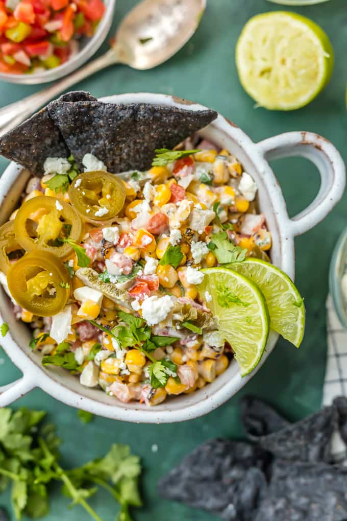 A bowl of Mexican street corn salsa with blue tortilla chips dipped in