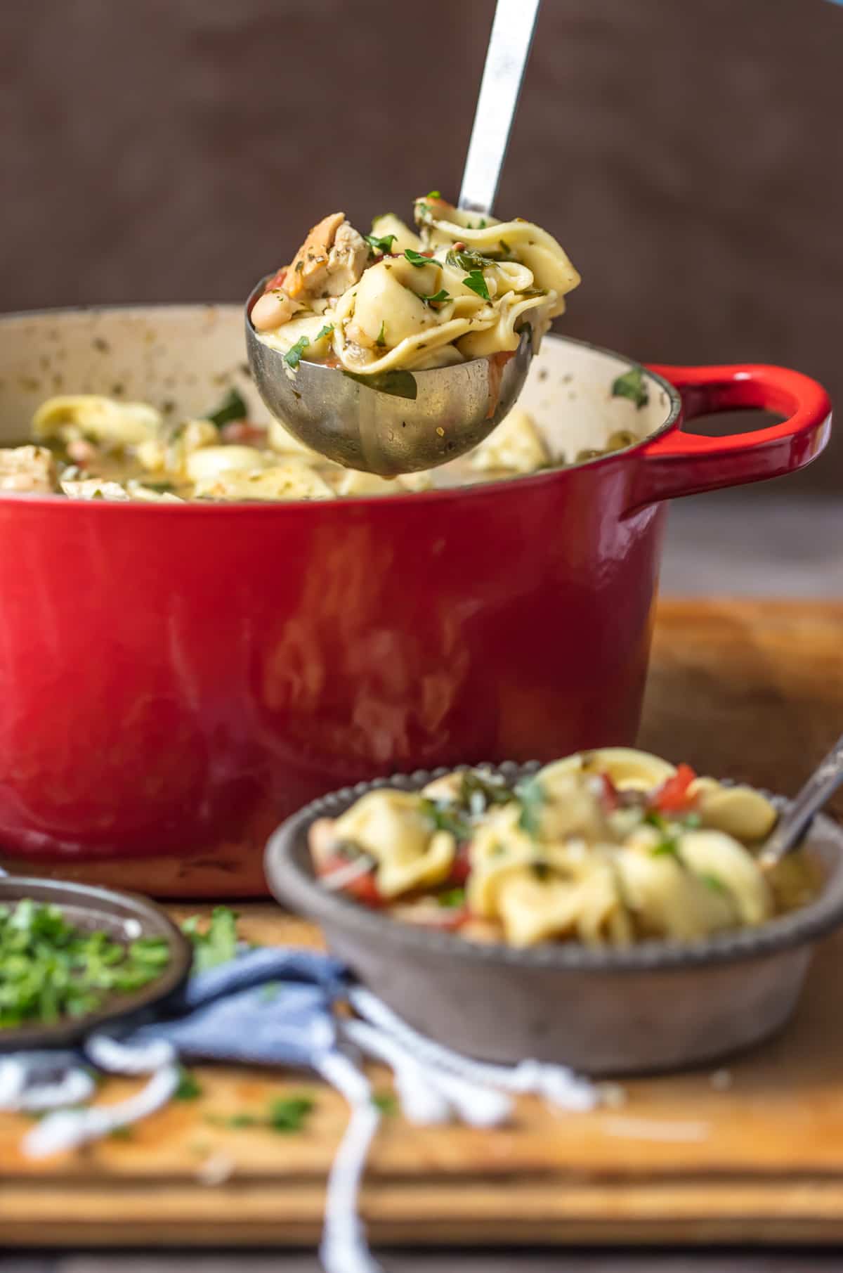 Red pot full of pesto chicken tortellini soup, next to a small bowl of soup