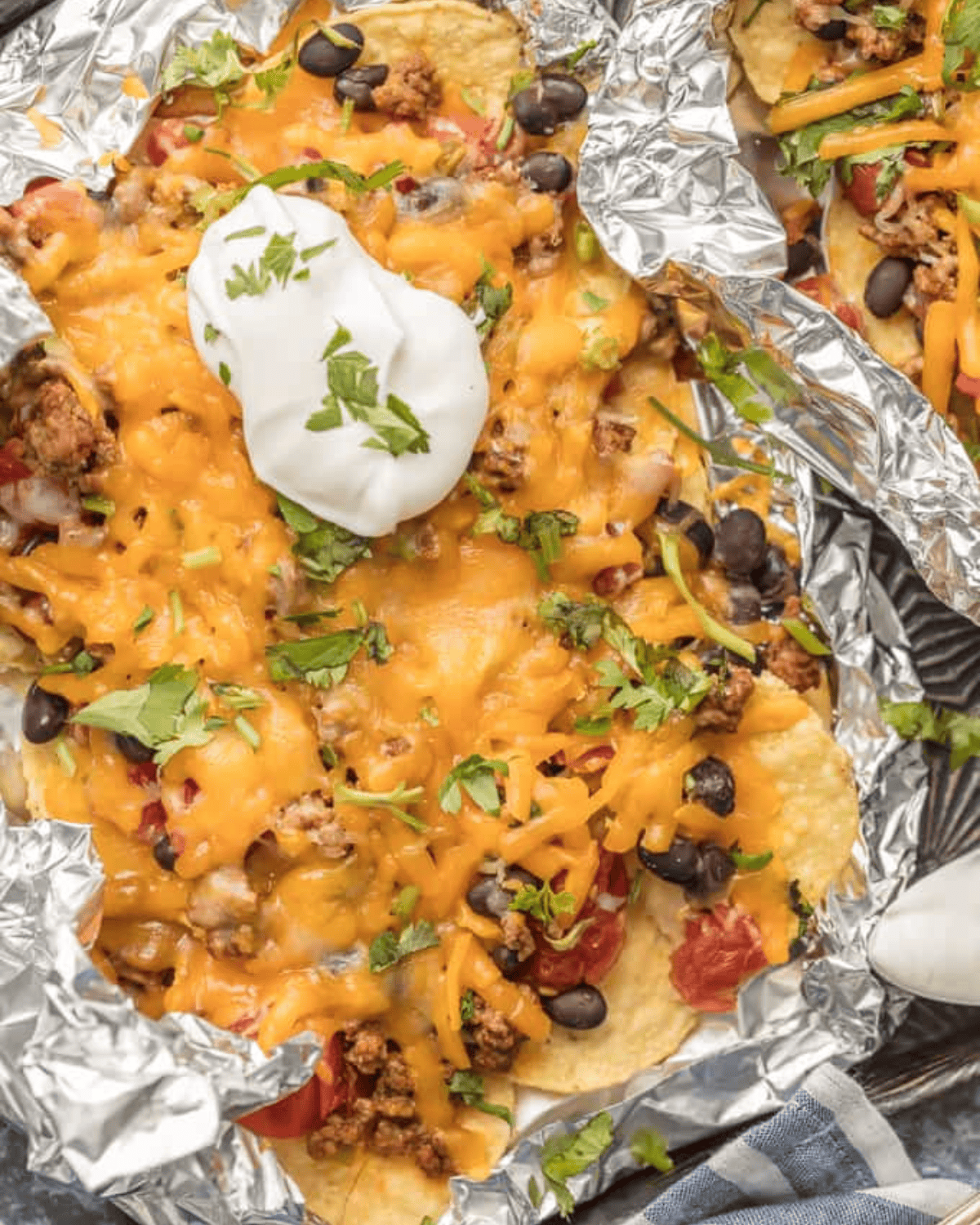 BEST Nachos Recipe - These foil packet nachos are loaded with beef, tomatoes, green chiles cheese, & more! I love this easy foil packet recipe, in the oven or on the grill. Foil packet nachos covered in cheese.