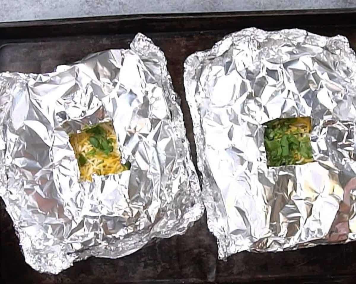 Two packets of foil packet nachos, vented, on a cookie sheet.