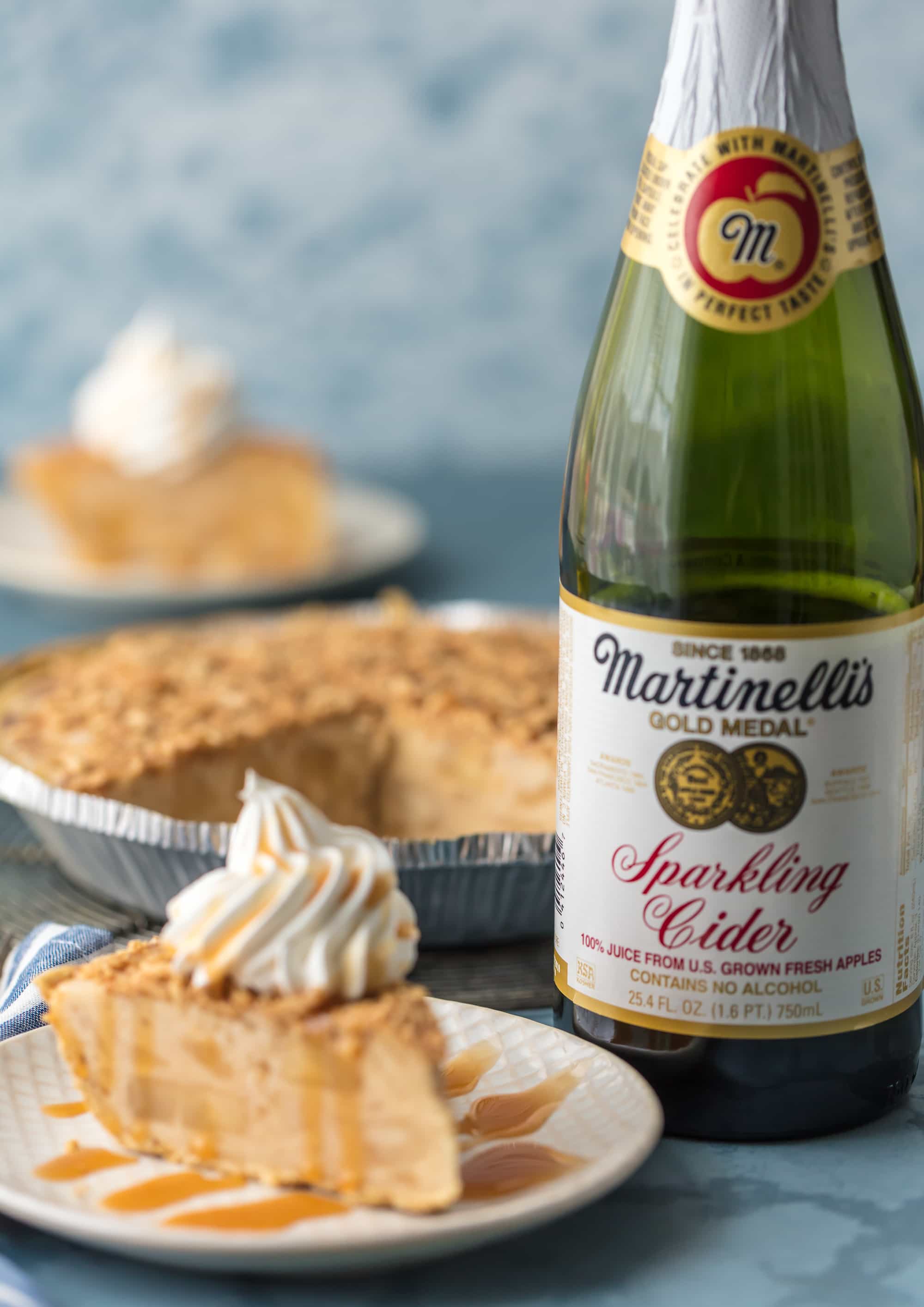 caramel apple freezer pie on plate topped with whipped cream with a bottle of martinelli's sparkling cider behind the plate
