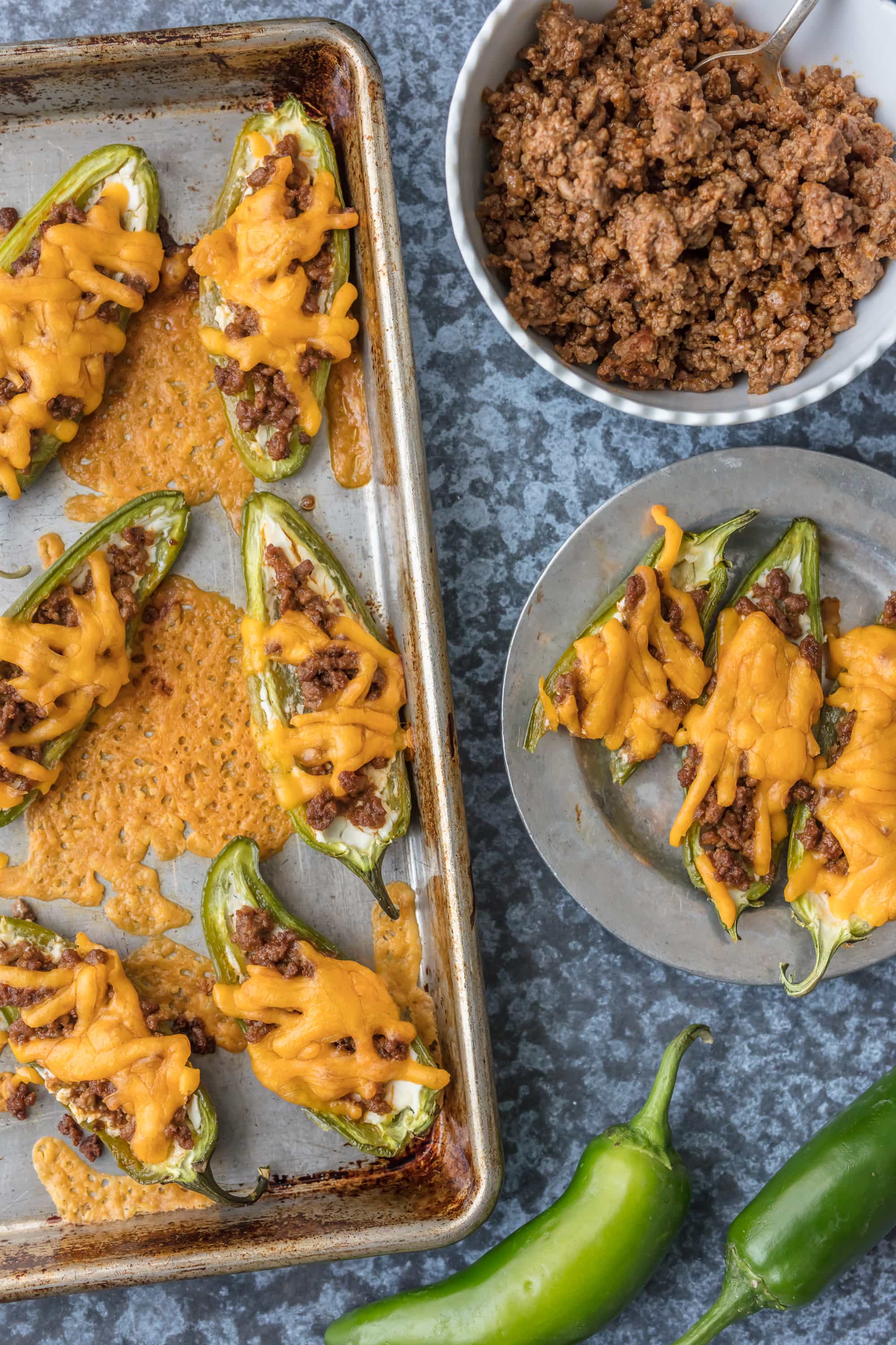 Stuffed jalapeno poppers on a baking tray, a plate, and a bowl of ground beef