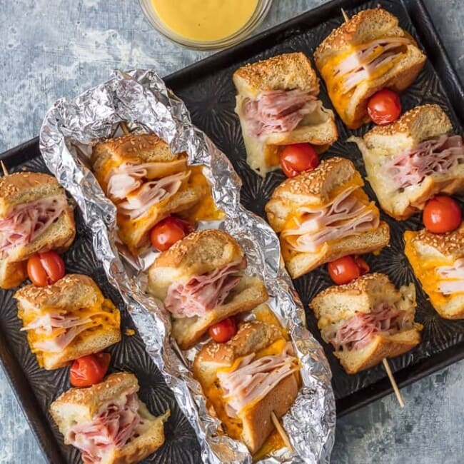 These Cheesy Garlic Butter Sandwich Skewers are a twist on an old classic. Cheesy Ham, Turkey, and Roast Beef sandwiches drizzled with garlic butter and cooked to perfection in foil packets; such a fun and delicious lunch or dinner!