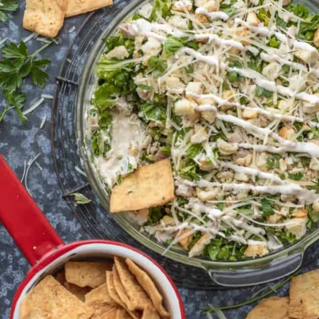 This CHOPPED CHICKEN CAESAR SALAD DIP is the ultimate fun and easy appetizer! We make this for tailgating, bbqs, potlucks, and more! Loaded with crisp lettuce, sour cream, caesar dressing, chicken, parmesan, croutons, and more!