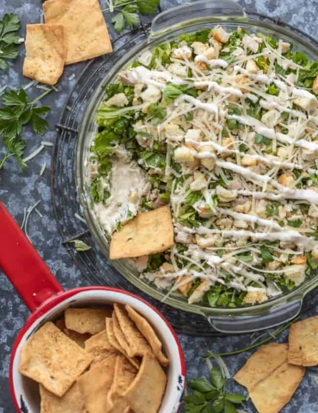 This CHOPPED CHICKEN CAESAR SALAD DIP is the ultimate fun and easy appetizer! We make this for tailgating, bbqs, potlucks, and more! Loaded with crisp lettuce, sour cream, caesar dressing, chicken, parmesan, croutons, and more!