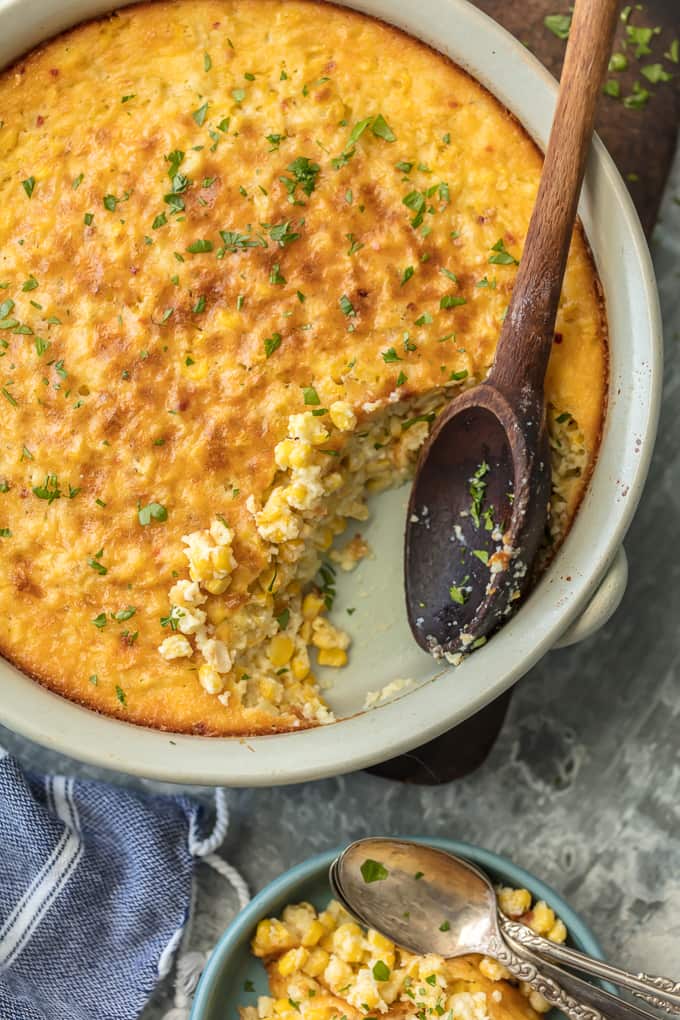 Corn Pudding recipe in white baking dish with a wooden spoon.