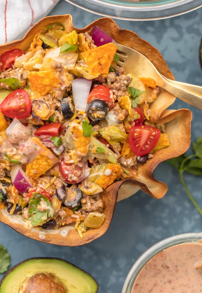 Taco Salad in tortilla bowl, filled with tomatoes, olives, onions, cheese