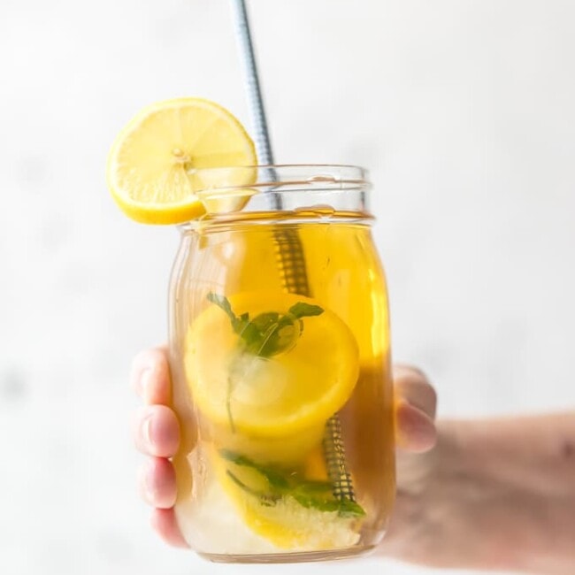 hand holding a mason jar of sweet tea with lemon mint simple syrup ice cubes and a straw