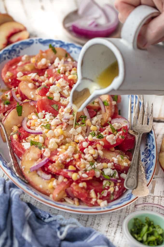 A homemade honey vinaigrette salad dressing being drizzled over corn and tomato salad