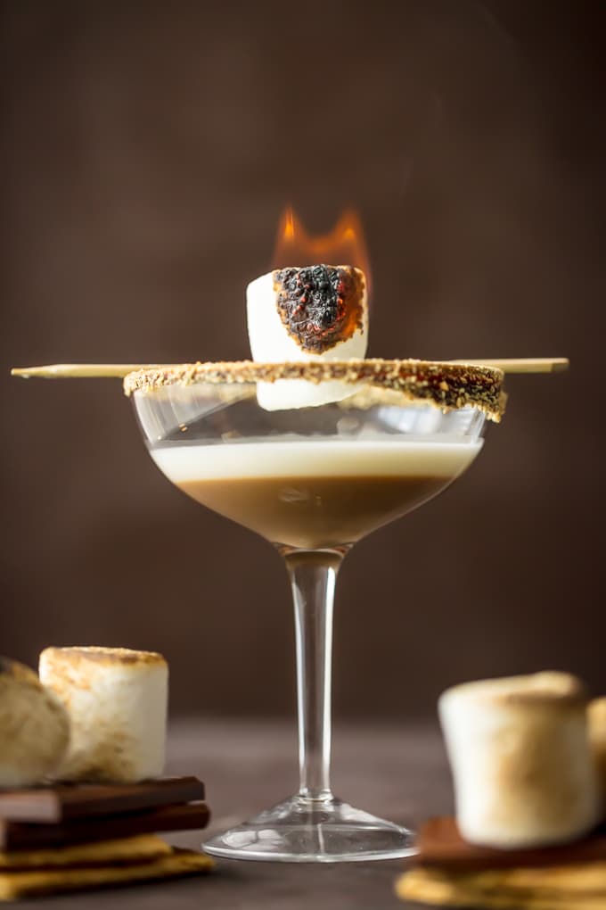 A flamed marshmallow sits on top of a smores martini glass