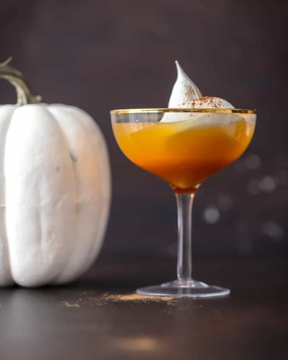 This Pumpkin Punch recipe is the perfect Thanksgiving or Halloween Punch idea. A fun & tasty Pumpkin Cocktail inspired by pumpkin pie! Glass of pumpkin pie punch with a white pumpkin next to it.