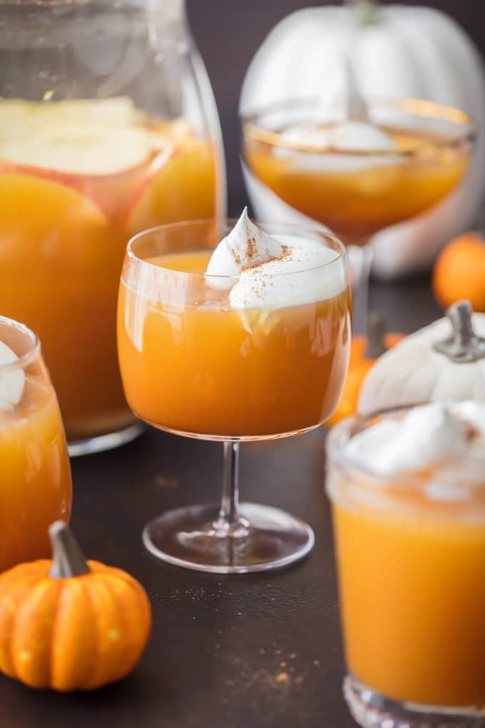 orange pumpkin pie punch in various sized glasses, with whipped cream topping.