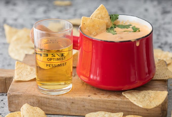 Beer cheese dip in red fondue pot, next to a glass of beer