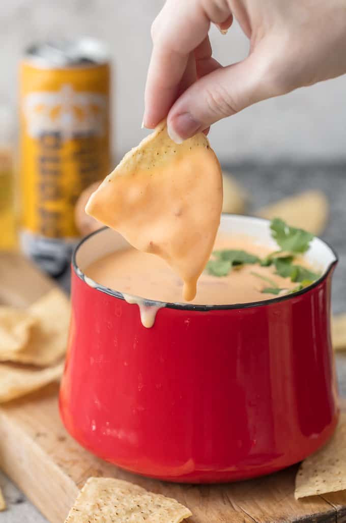 A tortilla chip dripping with beer cheese dip