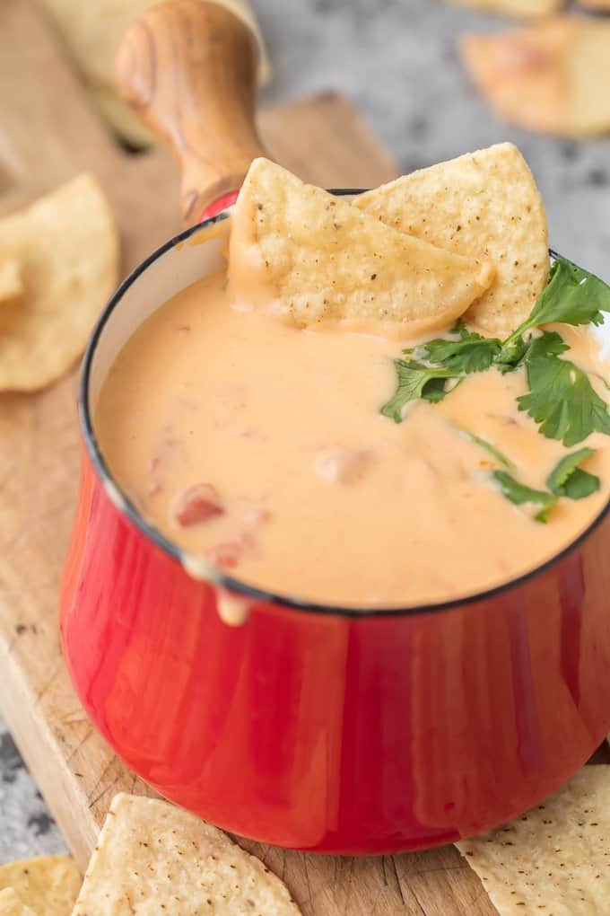 cheese dip in a red fondue pot with tortilla chips and cilantro.