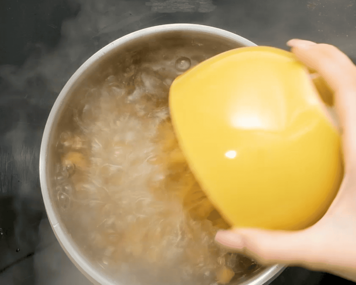 Pouring pasta from a yellow bowl into a of boiling water.