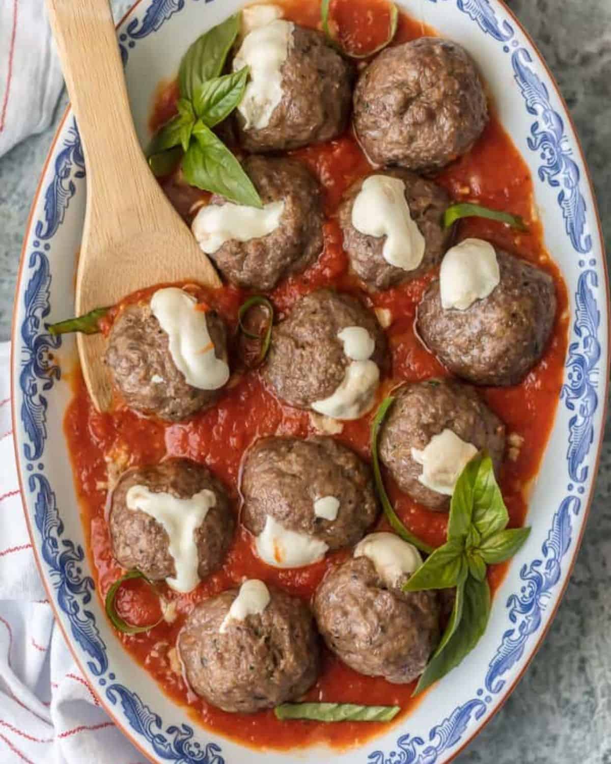 Mozzarella stuffed Italian Meatballs  in marinara sauce on a serving platter with a wooden spoon.