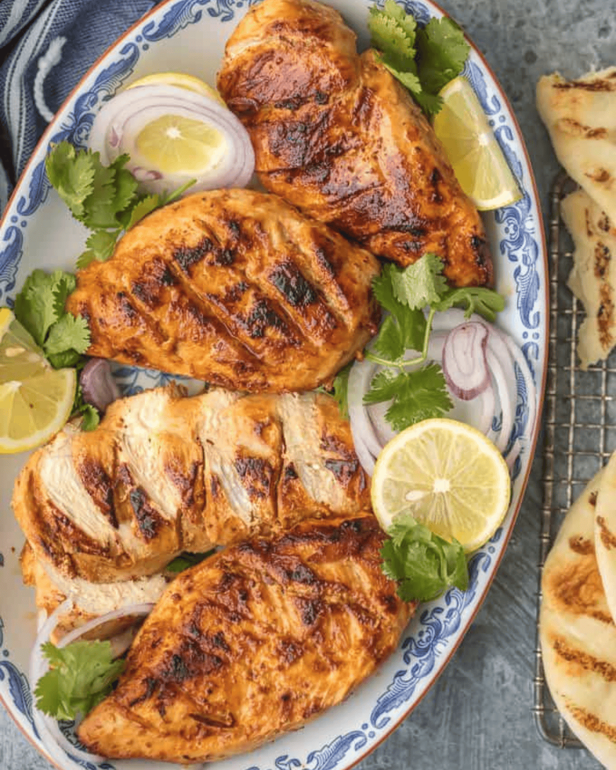 Tandoori chicken on a platter with red onions, lemon slices and cilantro.