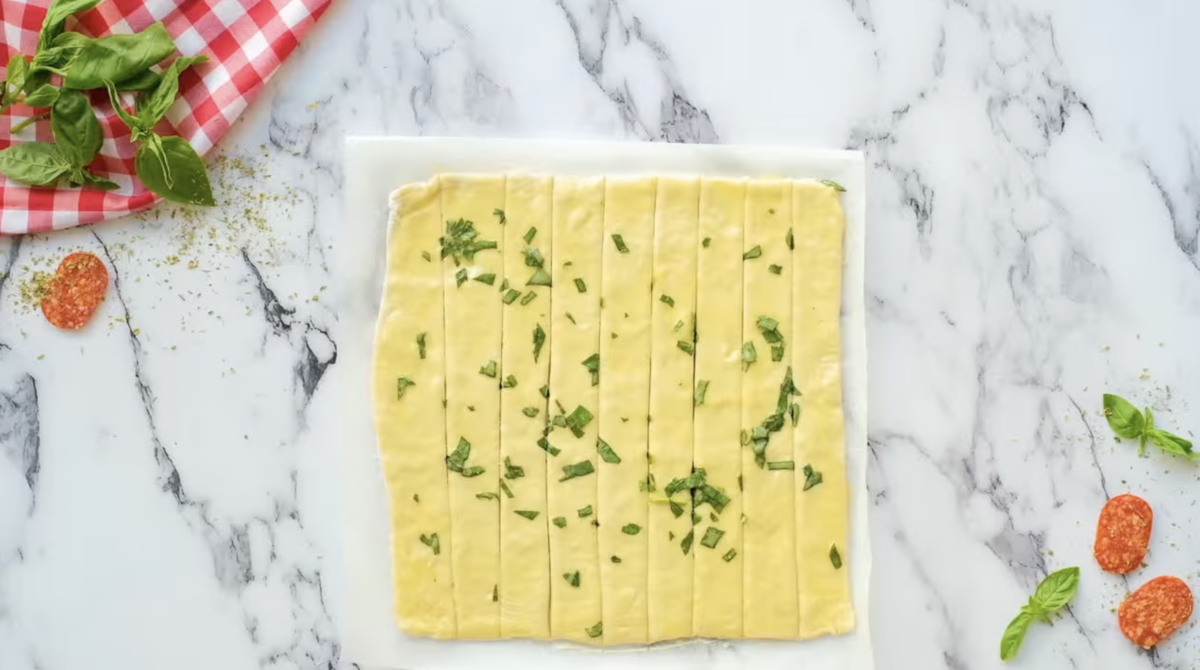 a square of pizza dough brushed with garlic basil butter and cut into vertical strips.