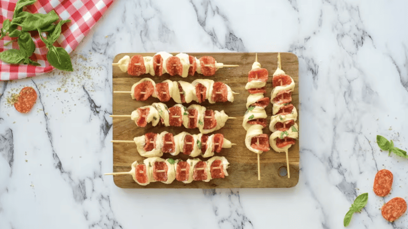 Pizza sticks with tomato and mozzarella on a wooden cutting board.